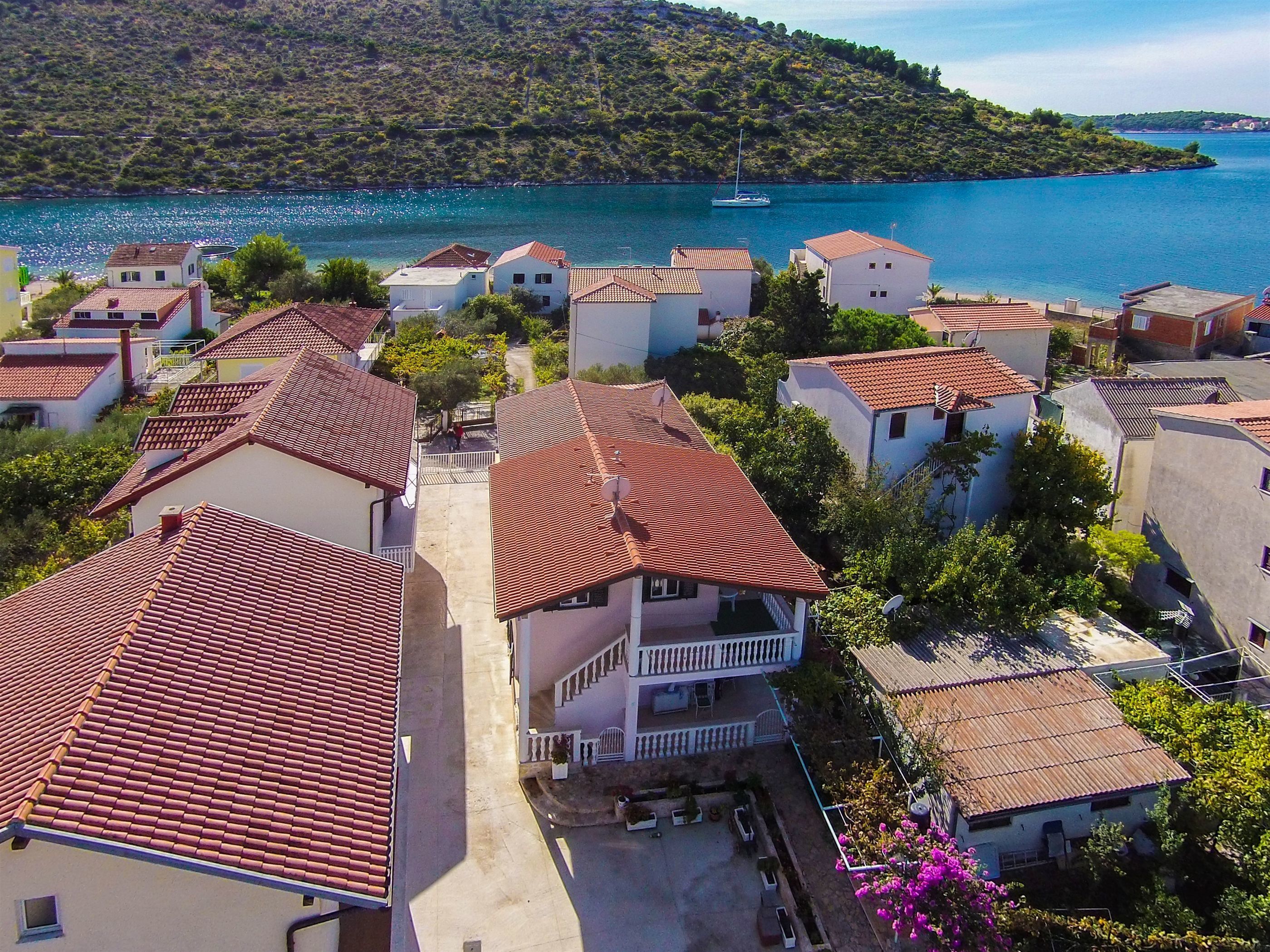 Ein Küstendorf mit Häusern mit Terrakotta-Dächern, einer zentralen Treppe, die zu einem Balkon führt, und Blick auf das Meer.