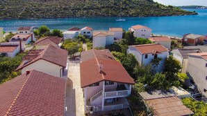 Un village côtier aux bâtiments aux toits de tuiles rouges, avec un escalier central menant à un balcon et une vue sur la mer.