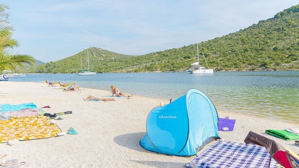 Une plage avec une tente, des serviettes et un bateau en arrière-plan.