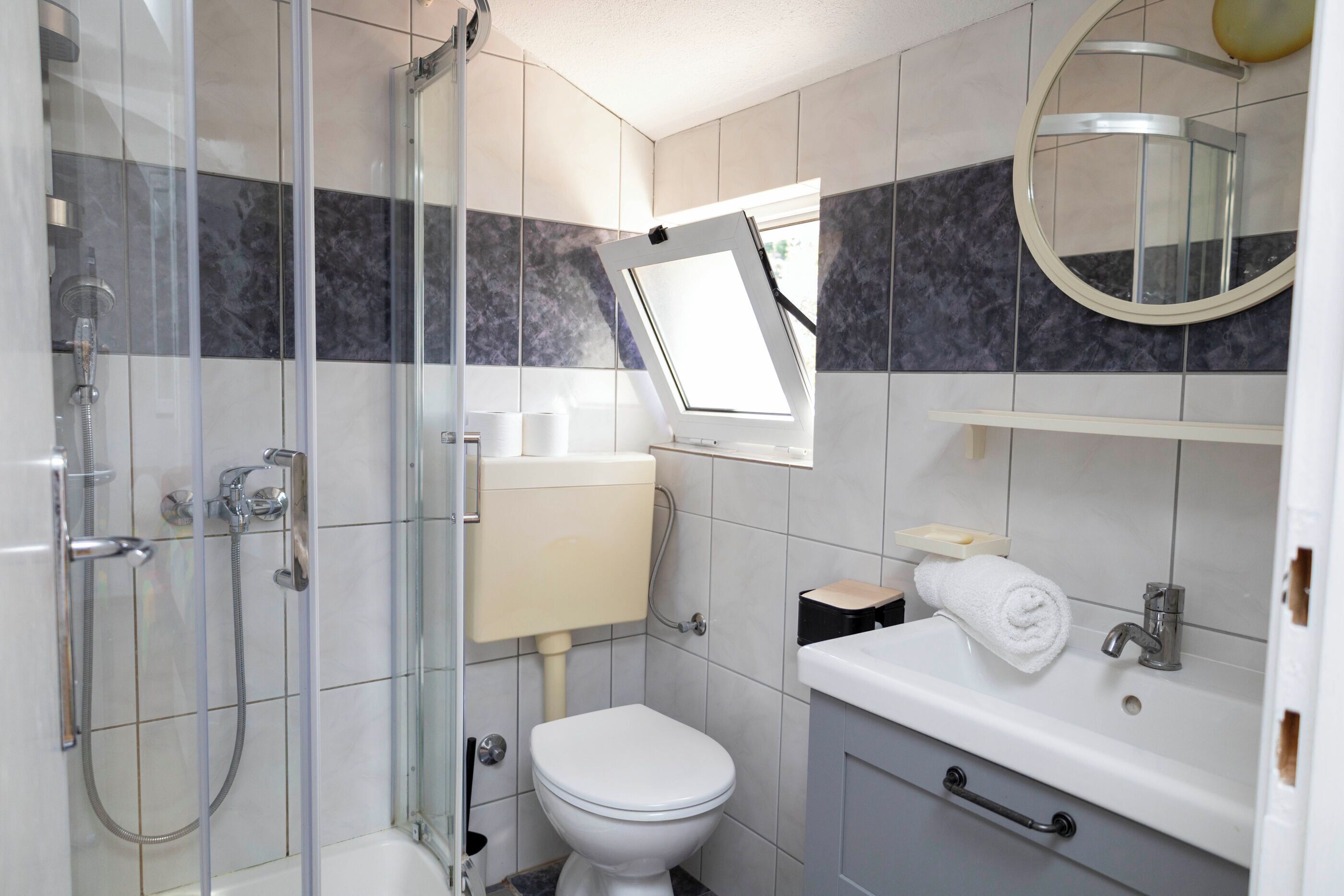 A bathroom with a glass shower enclosure, a toilet, a sink, and a mirror.