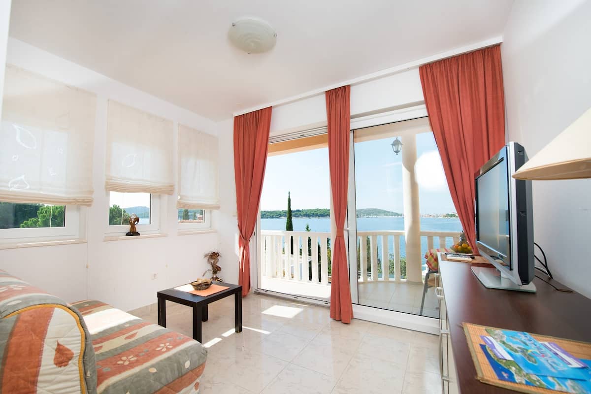 Ein Zimmer mit einer Couch, einem kleinen Tisch, einem Fernseher und einem Balkon mit Meerblick.