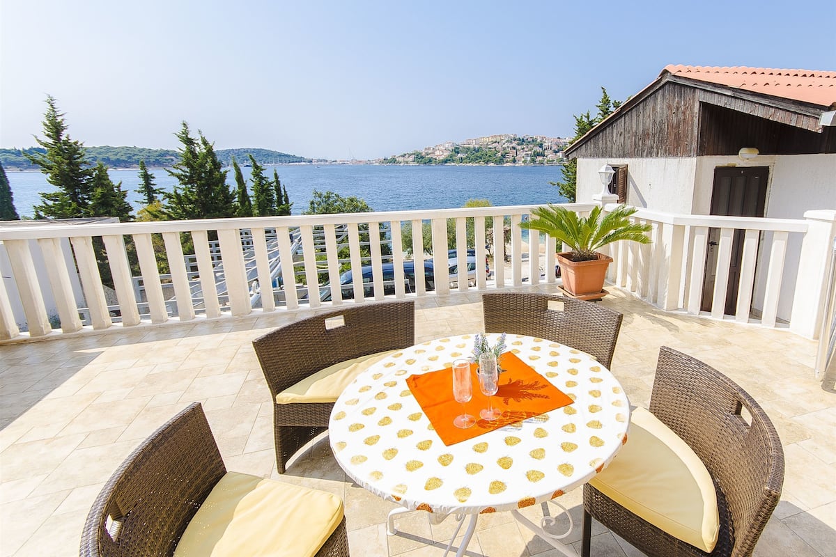 Ein Balkon mit Korbmöbeln, einem Tisch mit gemustertem Tischläufer und einem Blumentopf.