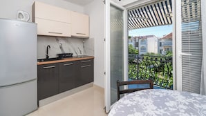 Una cocina moderna con refrigerador, estufa y armarios, un balcón con vista a casas vecinas, y un ventanal corredero.