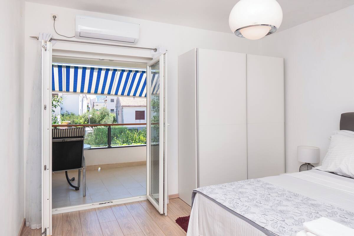A bedroom with a bed, a wardrobe, and a balcony with a striped awning.