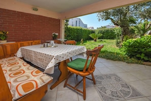Een terras buiten met een tafel, stoelen, een bakstenen muur en uitzicht op een tuin.