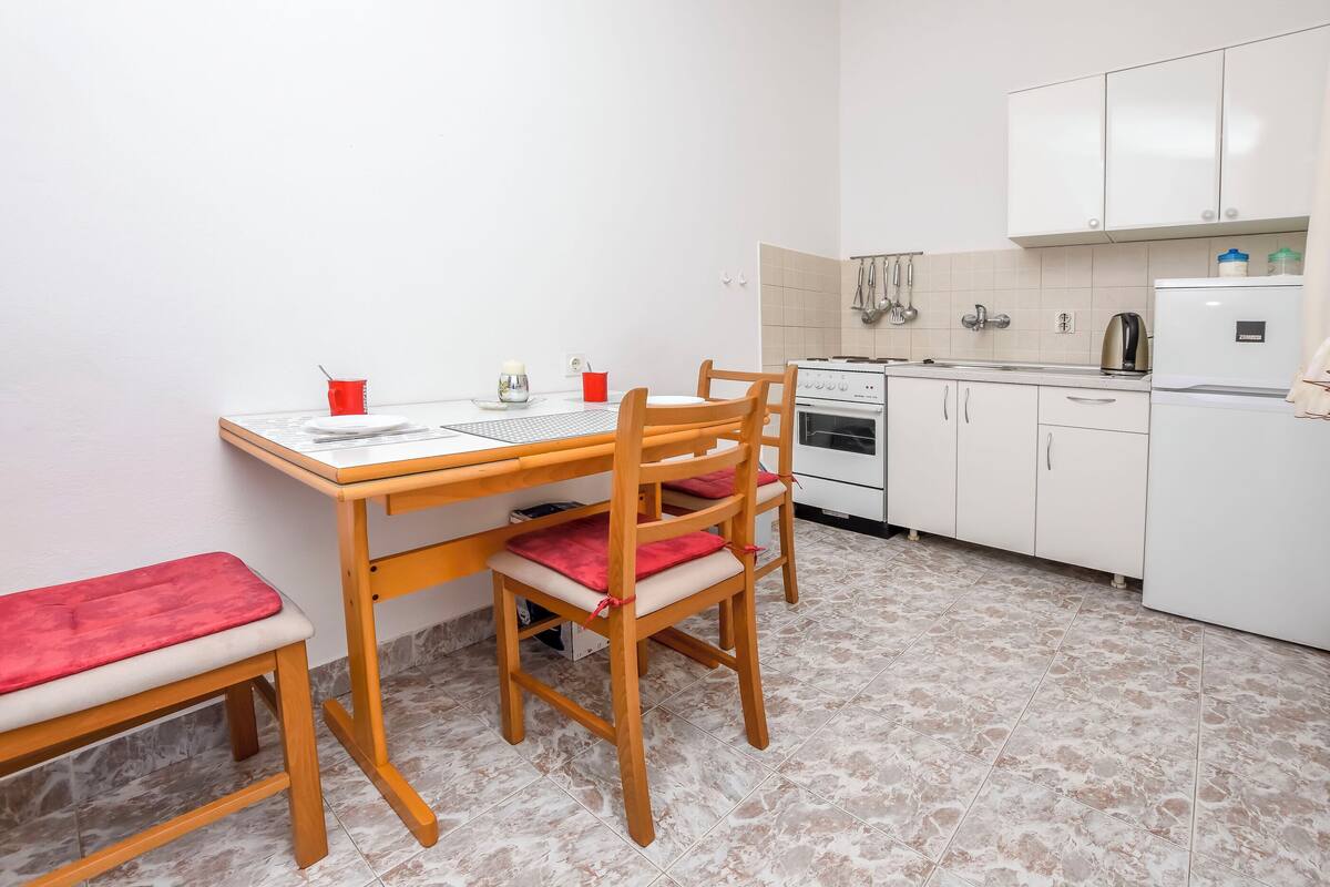 A compact kitchen with a dining table, chairs, a bench, a stove, and a refrigerator.