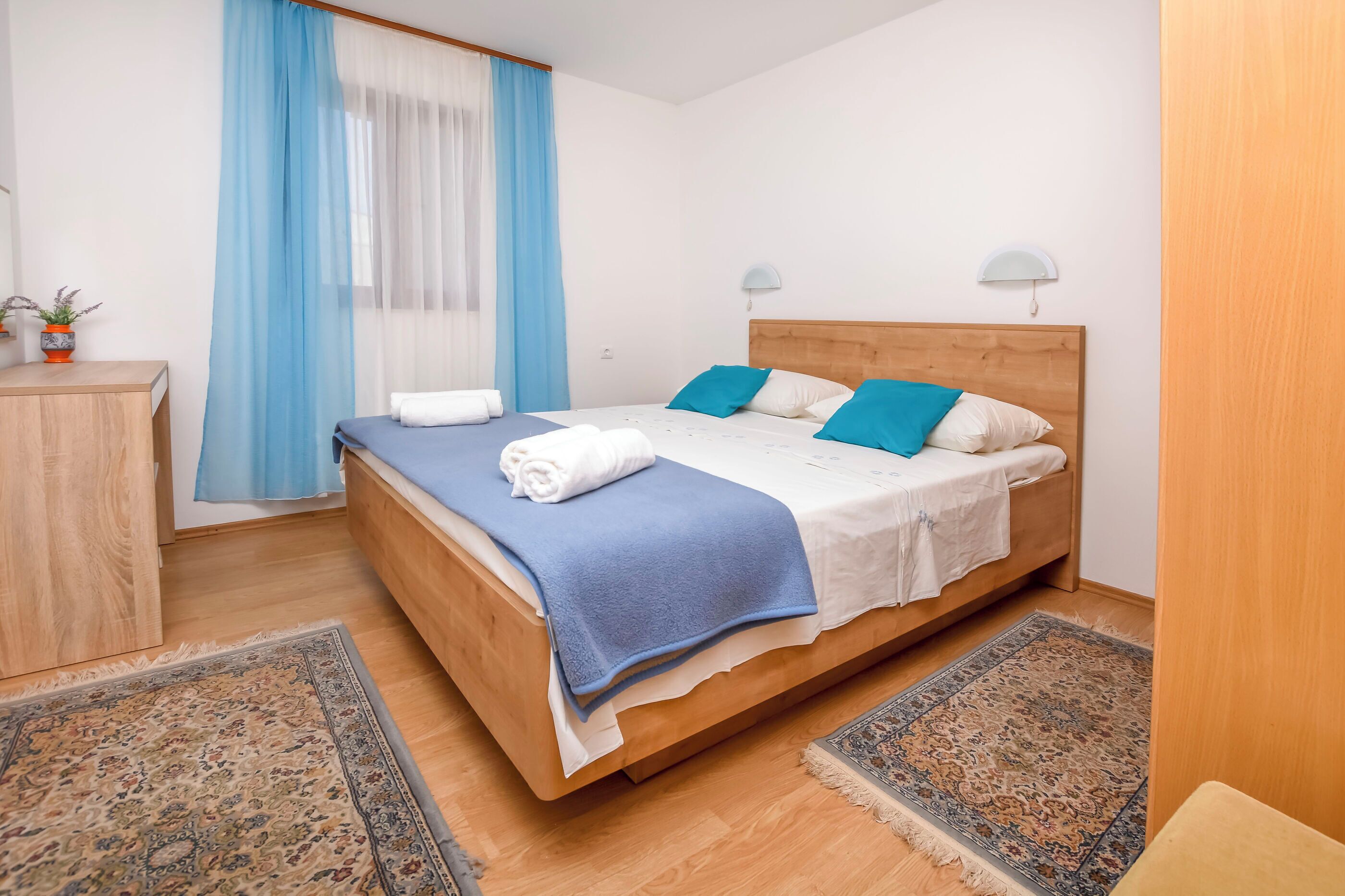 A neatly made bed with blue and white bedding, a wooden headboard, and two bedside lamps.