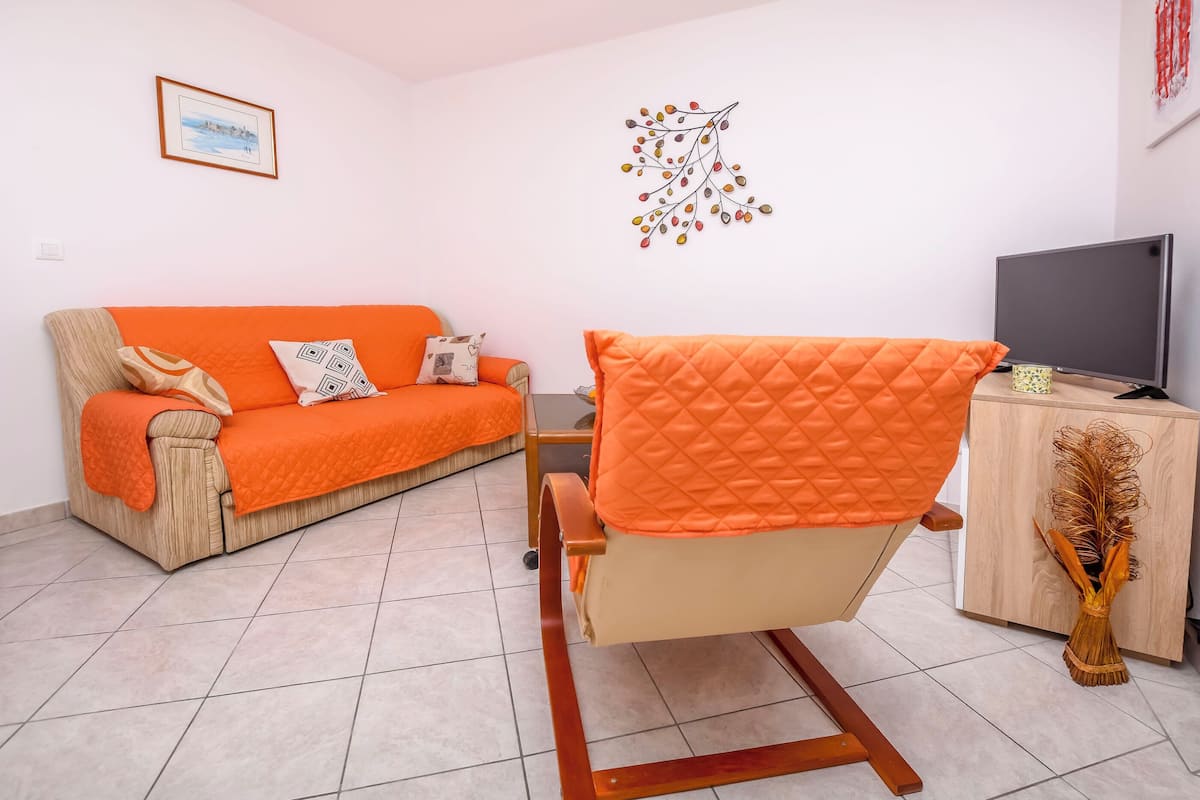 A living room with a beige sofa and an orange armchair, a wooden cabinet, and a television.