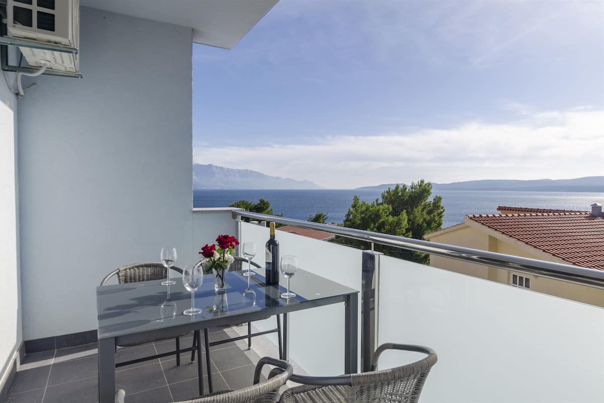 A balcony with a table set for two, overlooking a scenic view of the sea and mountains.