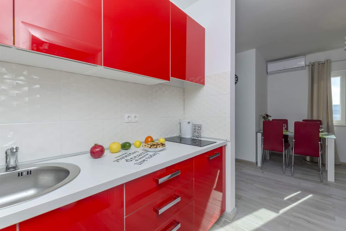 A modern kitchen with red cabinets, a white countertop, and a dining area with red chairs.