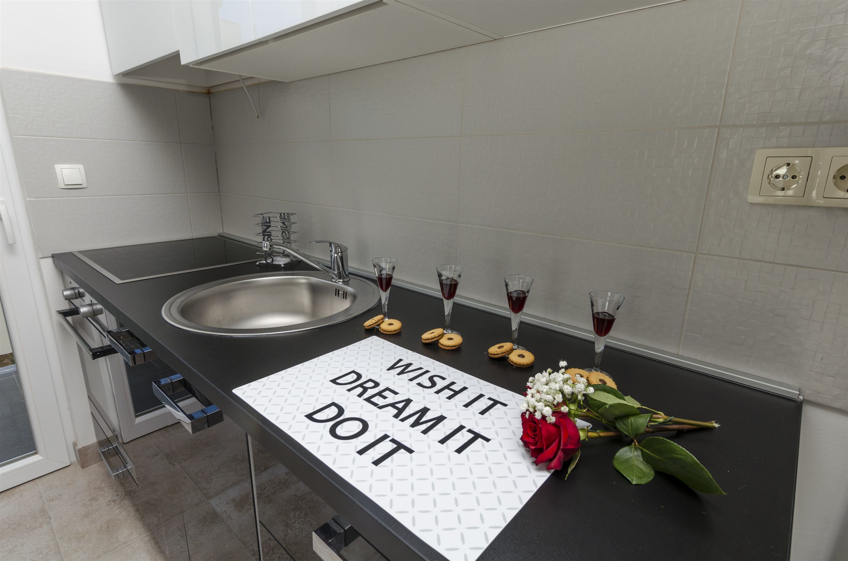 A modern kitchen with a stainless steel sink, a wine glass, and a decorative note on the counter.