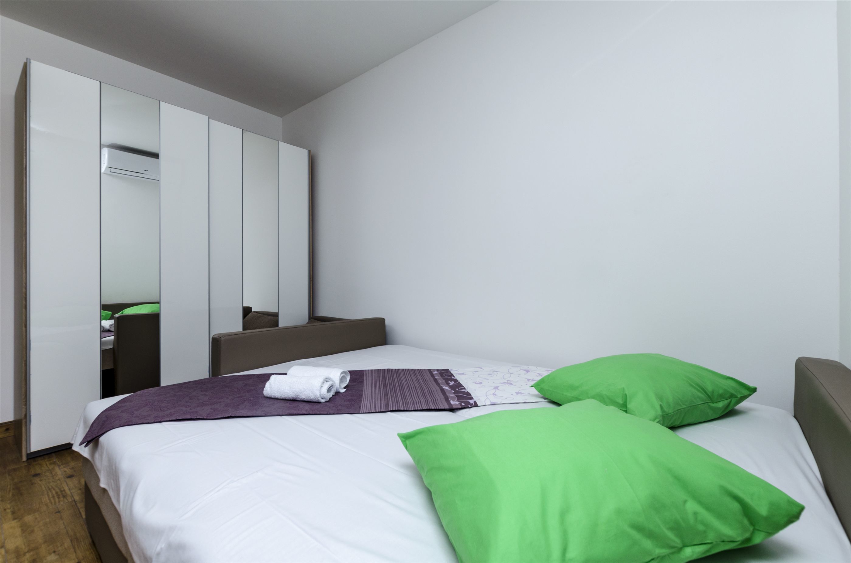 A modern hotel room with a bed, green pillows, a purple blanket, and a white headboard.