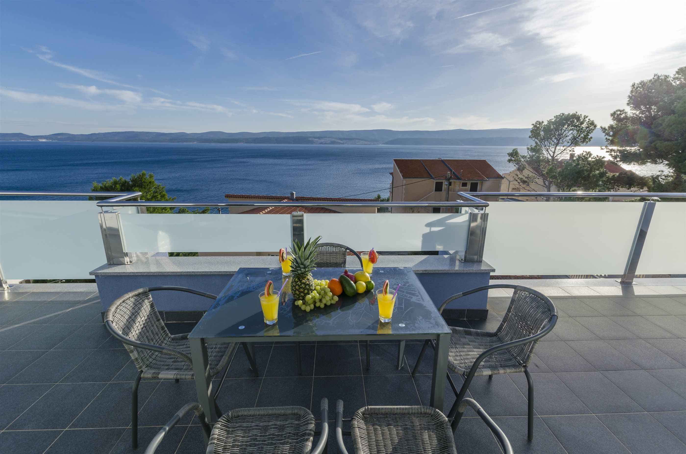 A terrace with a table set for two, a view of the sea, and a building in the background.