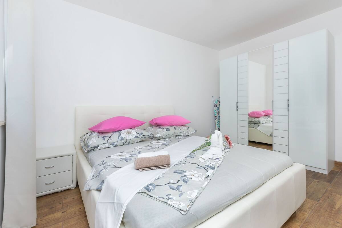 A bedroom with a bed, a nightstand, a wardrobe, and a mirror.