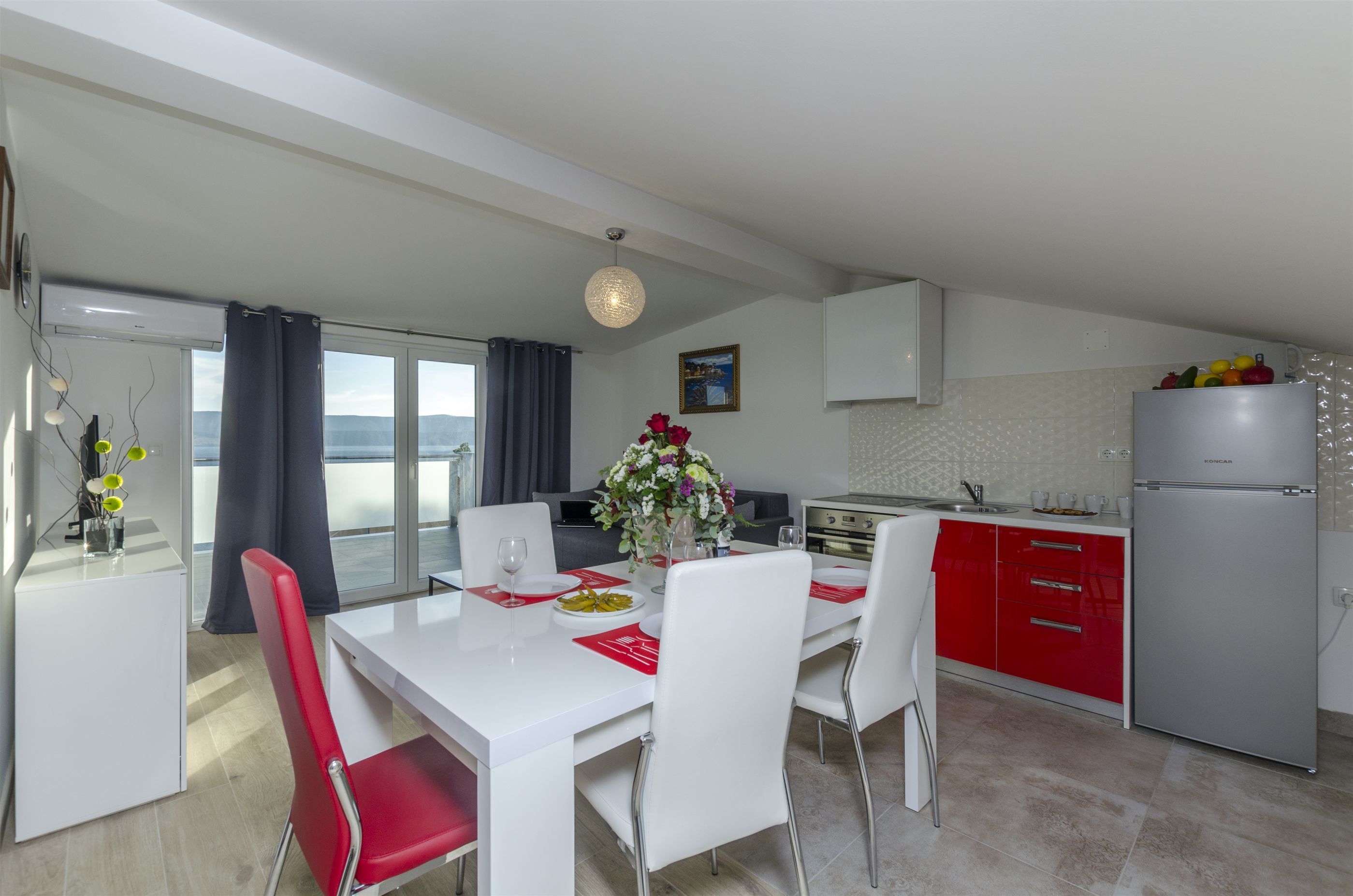 A modern kitchen with white cabinets, a stainless steel refrigerator, and a dining area with a white table and red chairs.