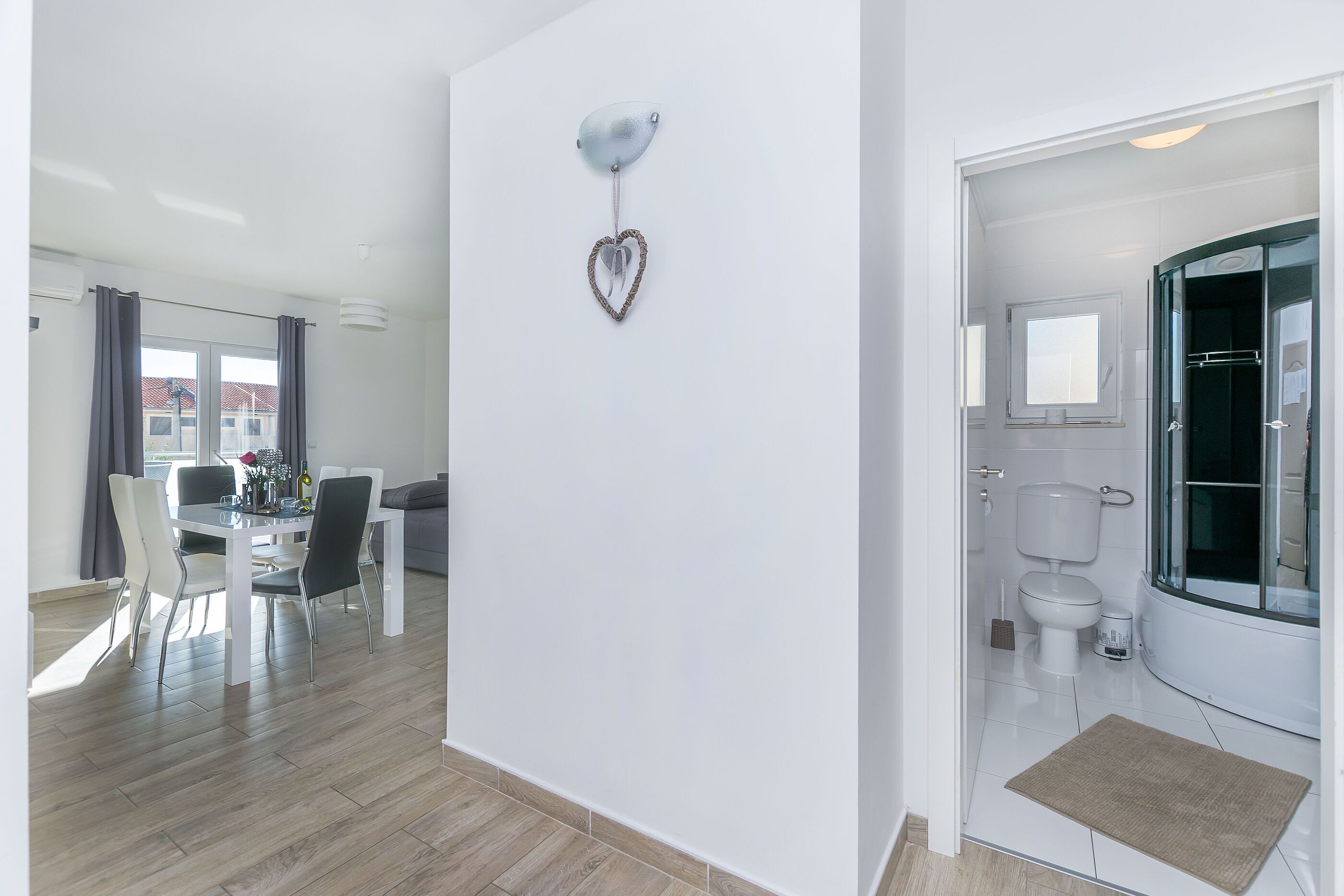 Ein moderner, gut beleuchteter Raum mit Essbereich, einer herzförmigen Dekoration an der Wand und einem Badezimmer mit Toilette und Dusche.