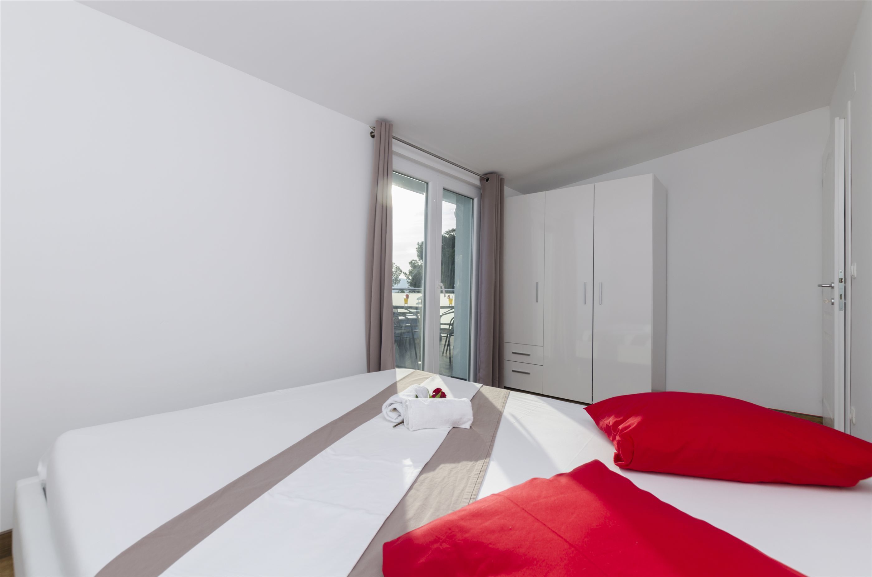 Een hotelkamer met een bed, een rood kussen, een witte handdoek en een schuifdeur naar een balkon.