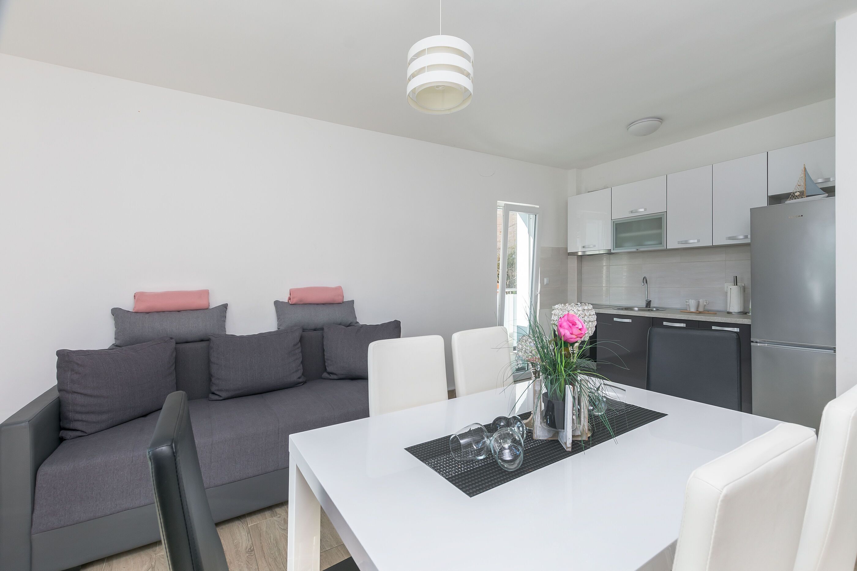 A modern kitchen with white cabinets, a stainless steel refrigerator, and a dining area with a white table and chairs.