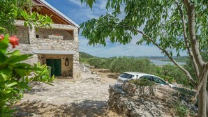 A stone house with a balcony, a stone pathway leading to the entrance, and a car parked nearby. - House Radojka (Tisno)