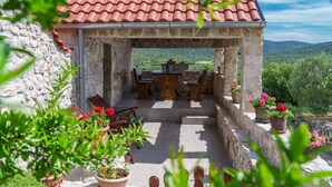 A stone patio with outdoor furniture and potted plants, overlooking a mountainous landscape. - House Radojka (Tisno)