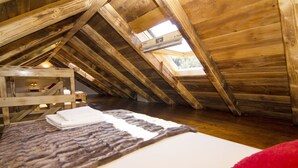 An attic bedroom with a sloped ceiling, wooden beams, a skylight, a bed with a fur throw, and a red pillow. - House Radojka (Tisno)
