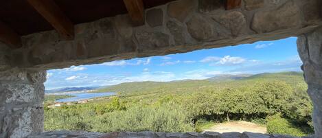 A stone-framed window overlooking a landscape with greenery and distant hills.