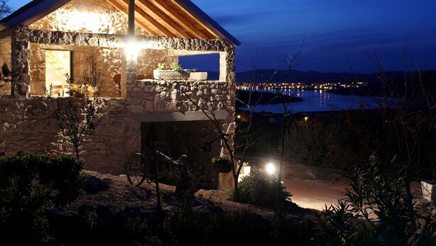 A stone house with a wooden roof and a view of a body of water at night. - House Radojka (Tisno)