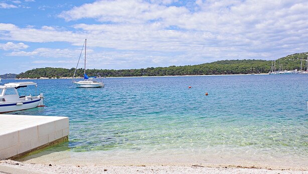 A coastal scene with boats docked, clear water, and a hilly landscape in the background. - Apartment Iryna (Rogoznica)