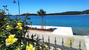 A coastal view with a clear sky, a body of water, and a paved walkway with yellow and white tiles. - Apartment Iryna (Rogoznica)