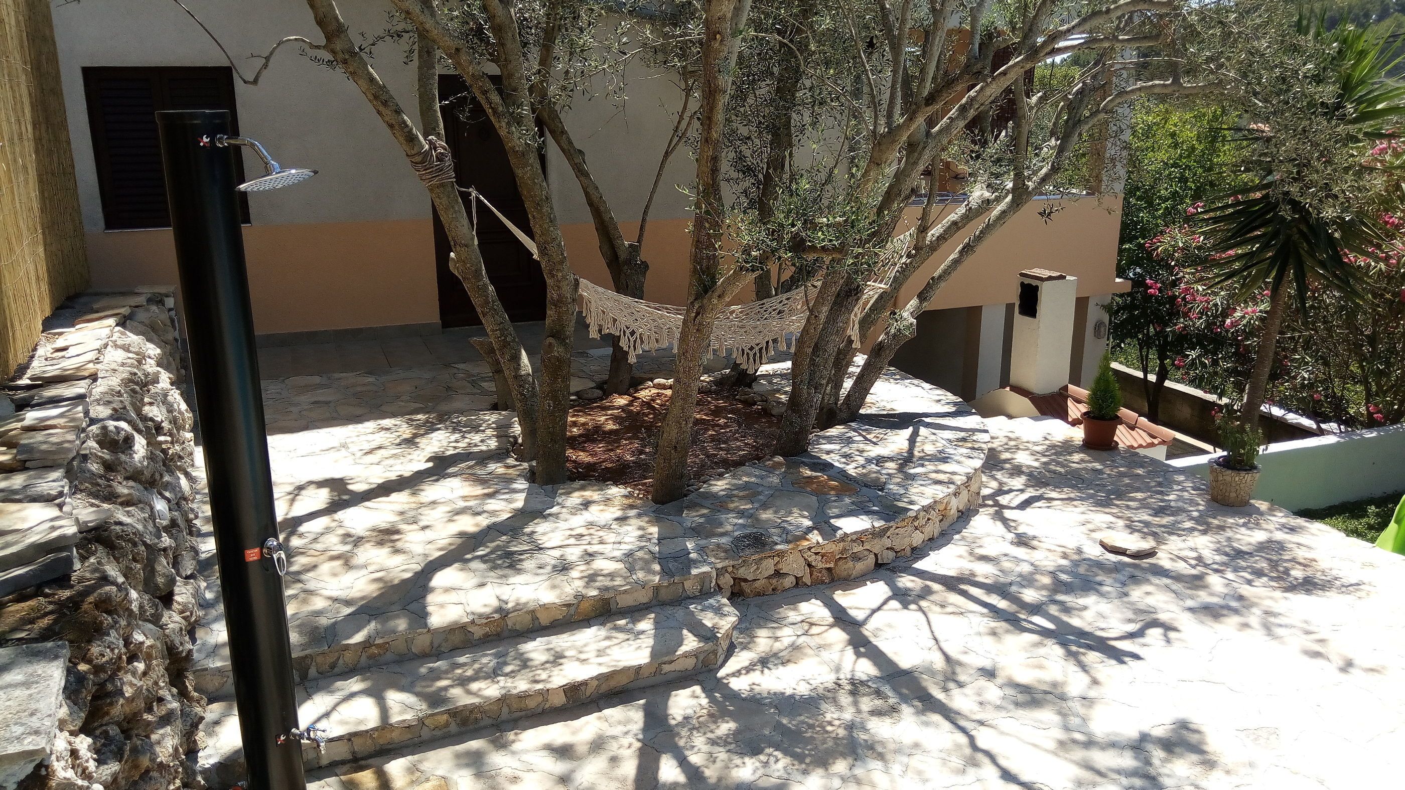 Un camí de pedra que porta a una cadira espanyola sota els arbres, amb una paret de pedra i una planta en test a la dreta.