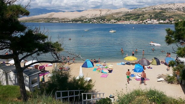 A beach with tents, umbrellas, and people swimming. - Apartments Ena (Pag)