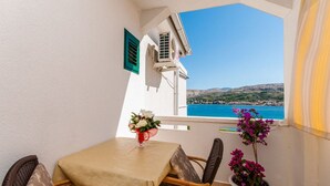A balcony with a table and chairs, a potted plant, and a view of the sea and hills. - Apartments Ena (Pag)