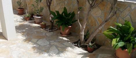 Un patio con baldosas de piedra, plantas en macetas y un muro de piedra.