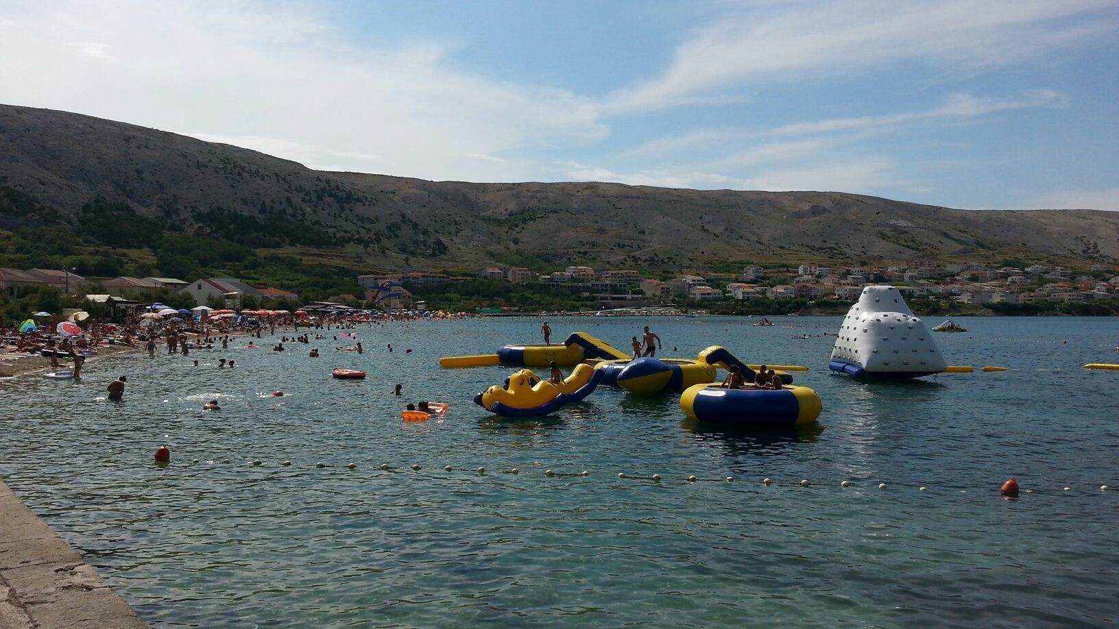 A crowded beach with inflatable water toys and people swimming.
