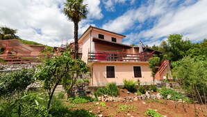 A two-story house with a balcony, surrounded by greenery and a clear sky. - Apartment Zorka (Medveja)