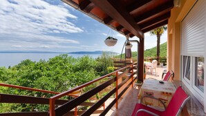 A balcony with a view of the sea and mountains, a table with chairs, and hanging planters. - Apartment Zorka (Medveja)