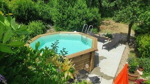 A wooden swimming pool with a ladder, surrounded by lush greenery and outdoor furniture. - Apartment Zorka (Medveja)