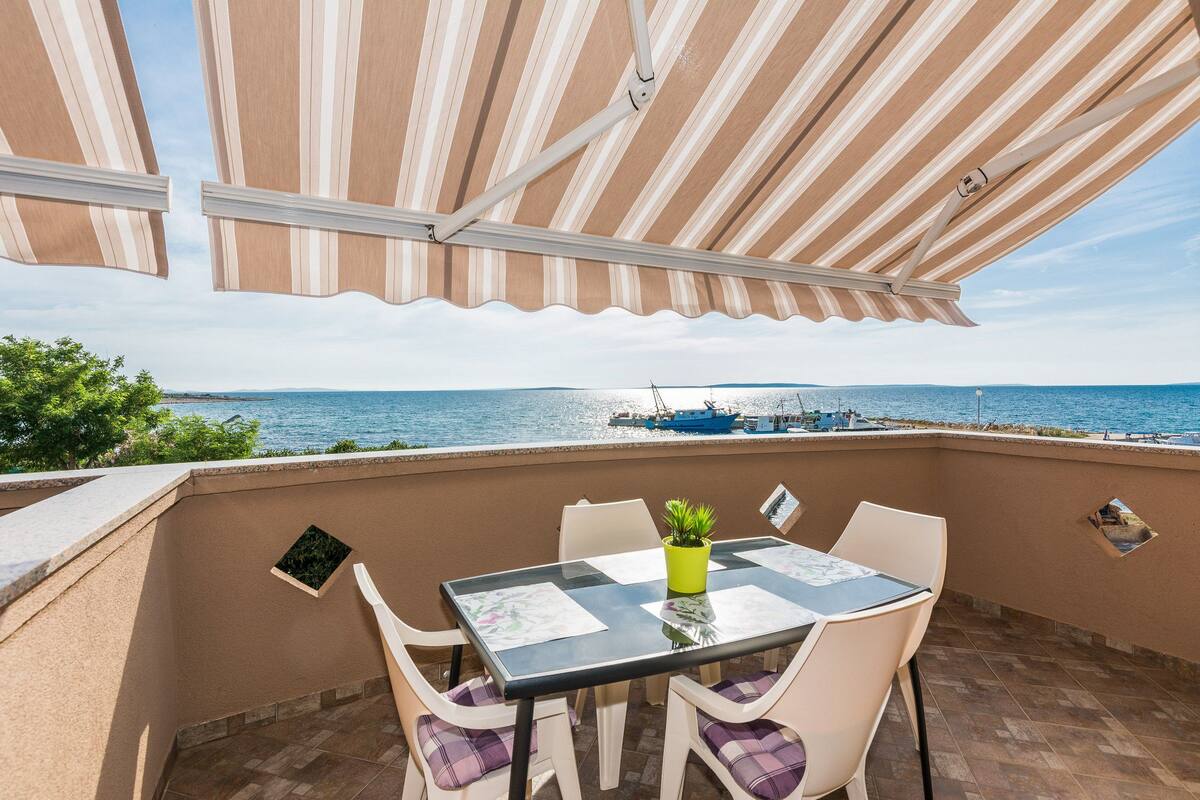 A balcony with a table and chairs, overlooking a body of water with boats.