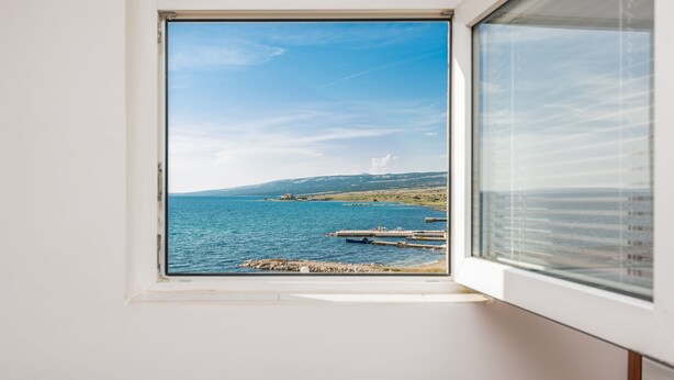 Una finestra amb una vista clara del paisatge costaner, incloent aigua, molls i turons llunyans.
