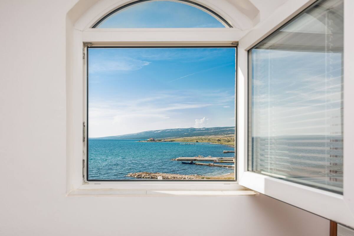 A window with a clear view of a coastal landscape, including water, docks, and distant hills.
