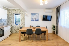 Ett modernt kök med vita skåp, ett matbord i trä med fyra stolar, en platt-TV och en krukväxt.