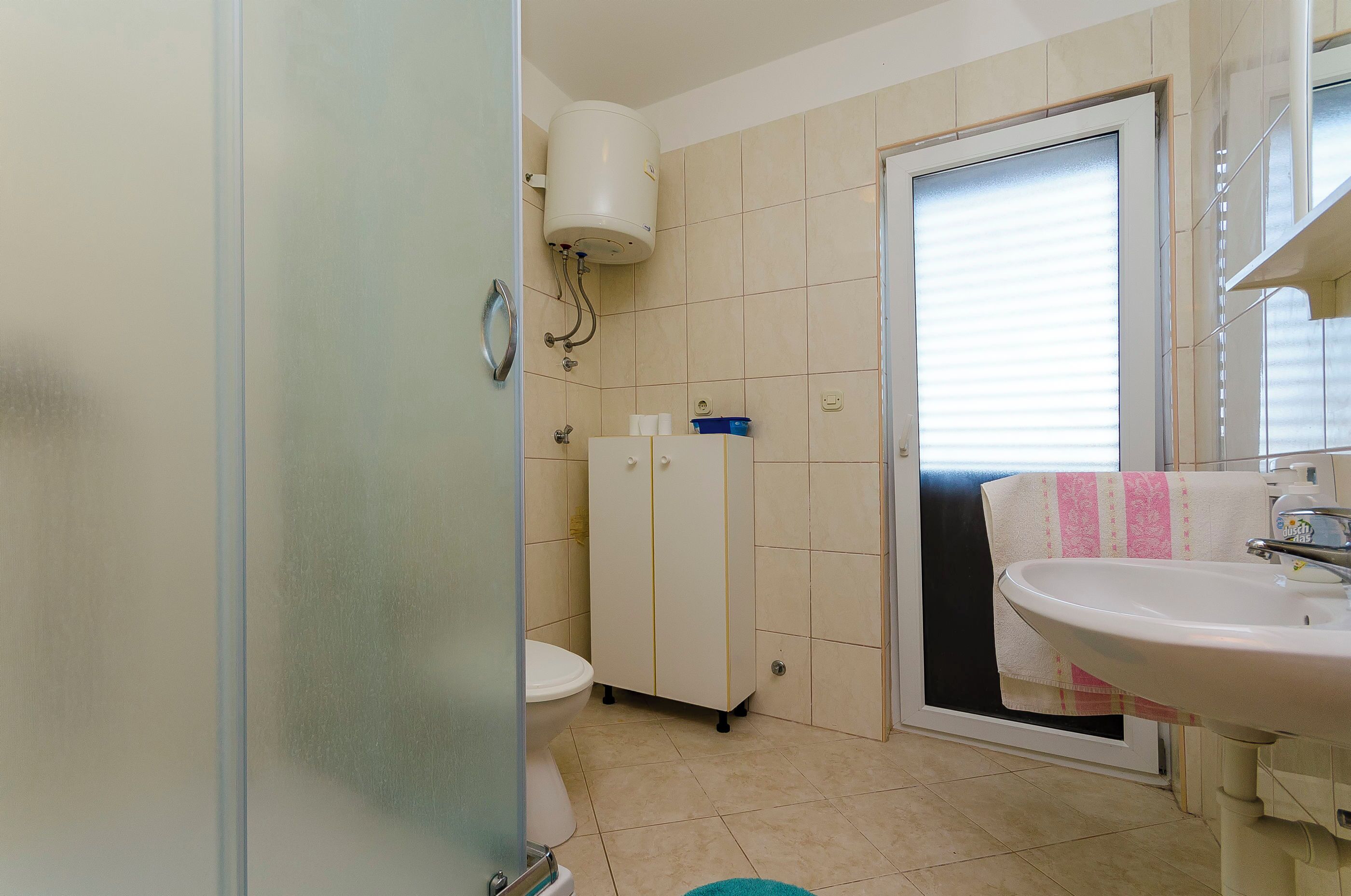 Et badeværelse med toilet, skab, vask og et håndklæde hængende på døren.