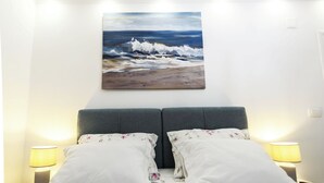 A bedroom with a large painting of a beach scene, two bedside tables with lamps, and a bed with floral bedding. - Apartments Milka (Slatine)