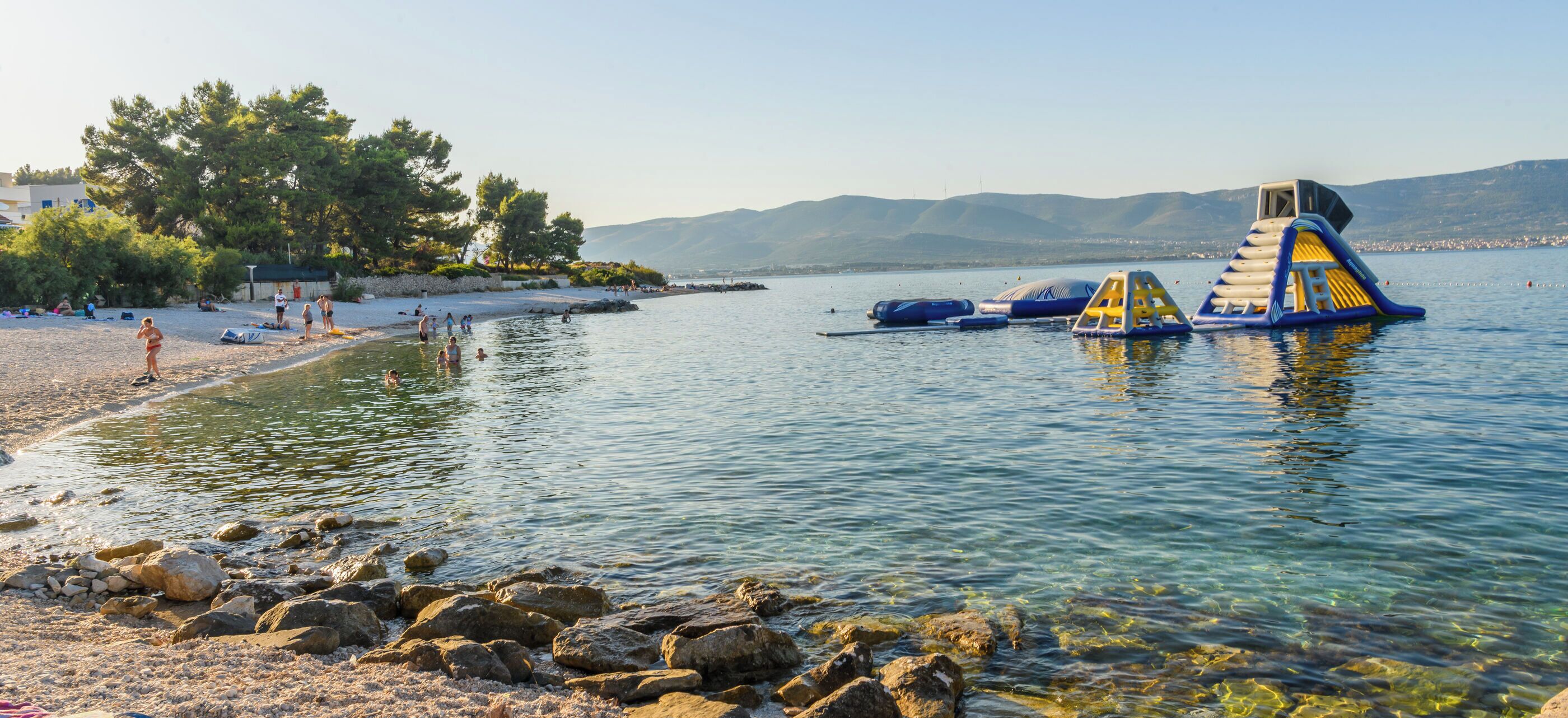 A beach with clear water, rocks, and inflatable water structures.