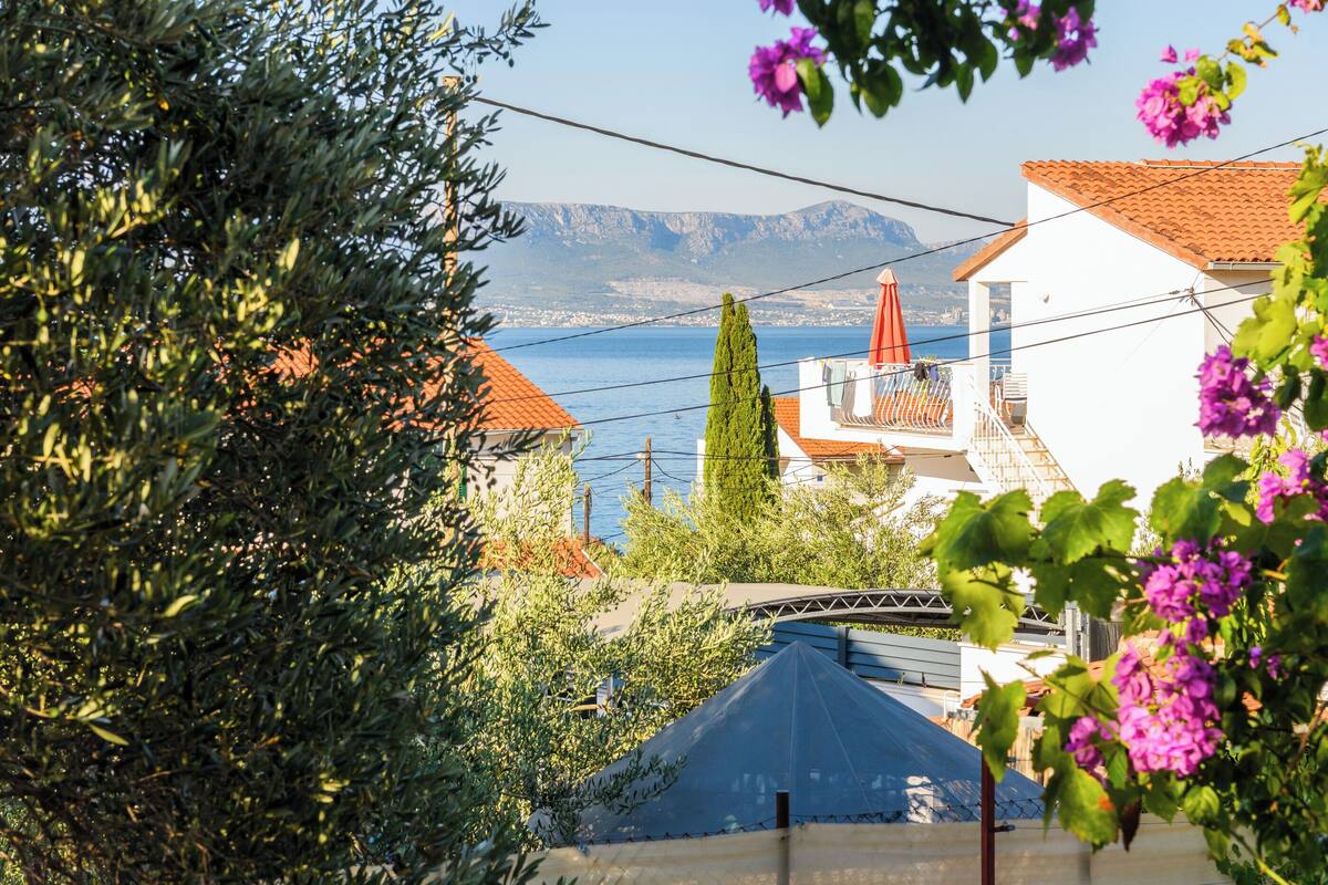 A coastal view with a clear blue sea, a mountain in the background, and a white building with a red roof.