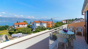 A balcony with a table and chairs, overlooking a coastal town with houses and a clear sky. - Apartments Milka (Slatine)