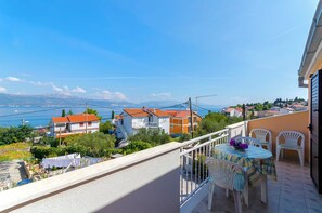 A balcony with a table and chairs, overlooking a residential area with houses and a distant view of the sea.