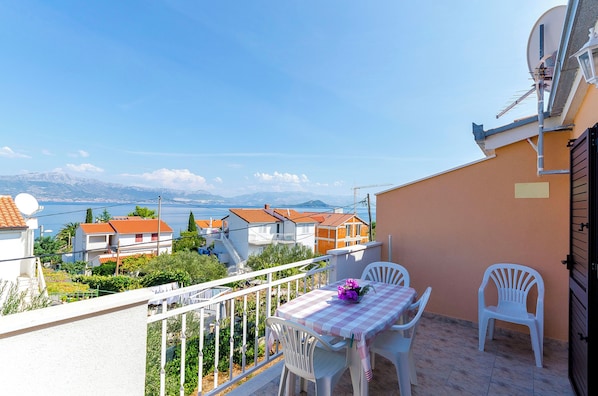 A balcony with a table and chairs, overlooking a residential area with houses and a body of water.