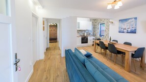 A modern living room with a blue sofa, a wooden dining table with chairs, and a kitchen in the background. - Apartments Milka (Slatine)