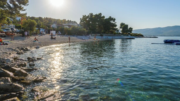 A beach with clear water, rocky shore, and a boat in the distance. - Apartments Milka (Slatine)